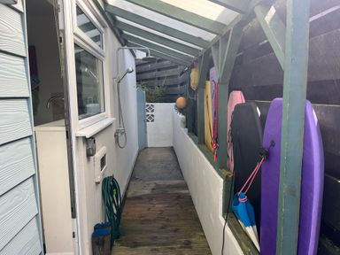 A covered outdoor corridor with an outdoor shower and bodyboards hanging on the wall at Atlantis in Polzeath