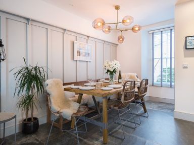 A dining room with a wooden table set for six with chairs and a vase of flowers at Albany in Port Isaac