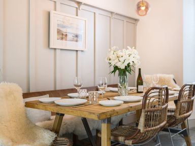 A dining room with a wooden table set with plates glasses and flowers surrounded by wicker chairs and sheepskin covers at Albany Port Isaac
