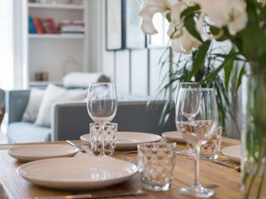 A dining table set with plates glasses and cutlery with a sofa and bookshelf in the background at Albany Port Isaac