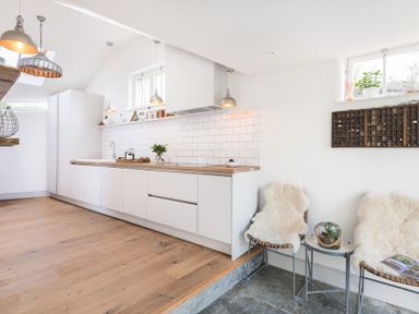 A kitchen with white cabinets wooden countertop pendant lights and two chairs with fur throws at Albany in Port Isaac