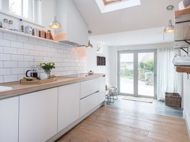 A kitchen with white cabinets wooden countertops white tiled backsplash and glass doors at Albany in Port Isaac
