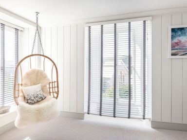 A hanging chair with a sheepskin and pillow near windows with blinds in a white room at Albany in Port Isaac