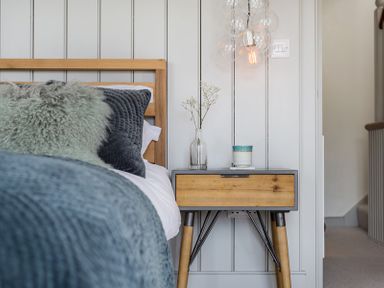 A bed with pillows next to a wooden bedside table with a vase and a cup at Albany in Port Isaac