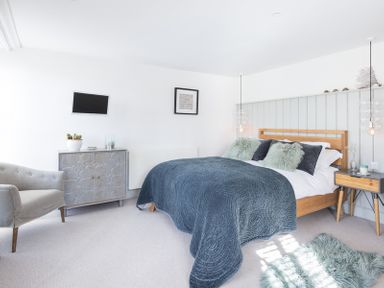 A bedroom with a bed a blue bedspread a gray armchair a cabinet a wall-mounted television and bedside tables at Albany in Port Isaac