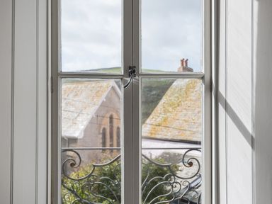 A window with decorative metal railing looking out to rooftops and a hillside at Albany in Port Isaac
