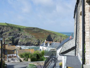A coastal village view with houses a road a patio with chairs and tables and green hills by the sea at Albany in Port Isaac