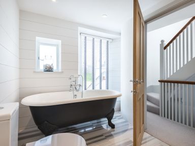 A bathroom with a clawfoot bathtub near windows and a staircase visible through an open door at Albany in Port Isaac