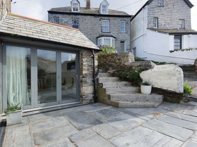 A stone patio with concrete steps and potted plants outside a building with large glass doors at Albany in Port Isaac