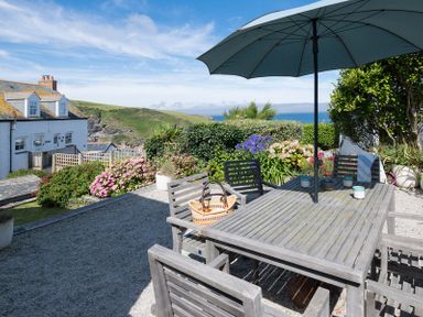 An outdoor patio with a wooden table and chairs under an umbrella surrounded by plants and flowers overlooking the sea at Albany in Port Isaac
