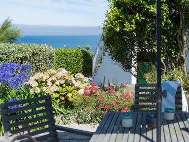 Outdoor garden area with wooden table and chairs overlooking hedges flowers and the sea at Albany in Port Isaac