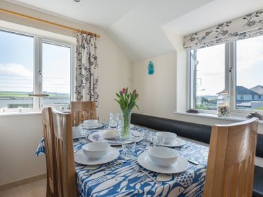 A dining area with a table set with white bowls and glasses in front of windows at Polmorla in Polzeath