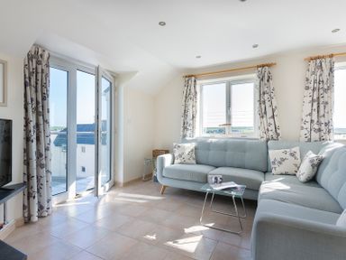 A living room with light blue sofa and floral curtains near windows and glass door at Polmorla in Polzeath