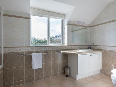 A bathroom with a window a sink with a cabinet a mirror a towel on a rail and tiled walls at Polmorla in Polzeath