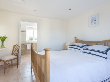 A bedroom with a wooden bed a chair a lamp and a door leading to a bathroom at Polmorla in Polzeath