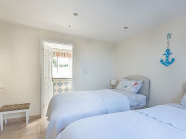 A bedroom with two single beds a bench near a door leading to a bathroom at Polmorla in Polzeath