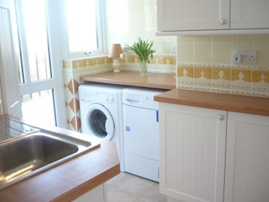 A kitchen with a sink washing machine dishwasher and wooden countertops at Polmorla in Polzeath