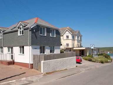 A street view with two buildings a red car and a coastline in the background at Polmorla in Polzeath