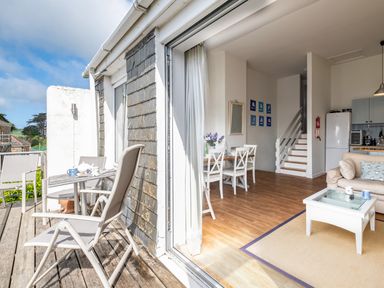 An open patio door showing a balcony with chairs and a table and an interior with a dining table and chairs a sofa and a coffee table at Slipway 12 in Rock