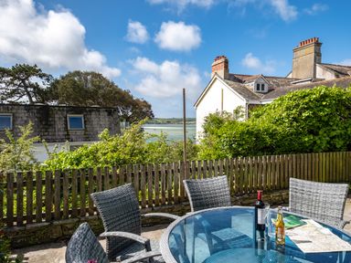 An outdoor patio area with a glass table and four chairs overlooking a wooden fence and neighboring houses at Slipway 12 in Rock