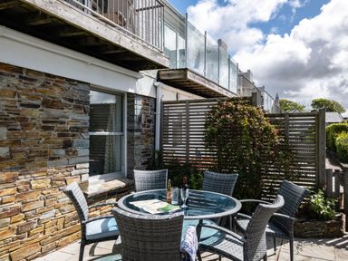 An outdoor patio with a round glass table and six wicker chairs next to a stone wall at Slipway 12 in Rock
