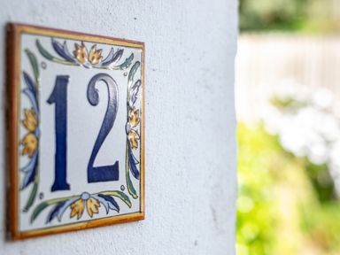A ceramic house number 12 plaque on a white wall with a blurred garden background at Slipway 12 in Rock