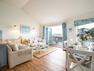 A living room with beige sofas a coffee table and a dining table set with flowers and dishes at Slipway 12 in Rock