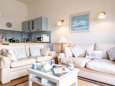 A living room with beige sofas pillows a white coffee table with a teapot and mugs and a kitchen area at Slipway 12 in Rock