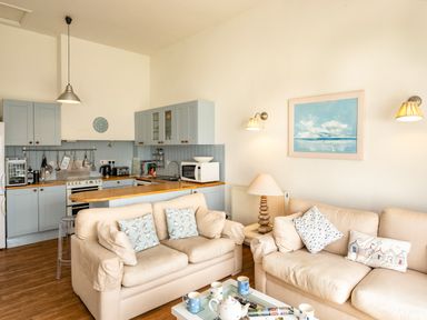 An open plan living area with beige sofas pillows a coffee table and a kitchen with blue cabinets at Slipway 12 in Rock