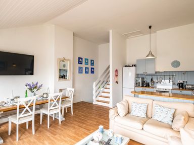 An open living space with a dining table and chairs a sofa with cushions a kitchen area and stairs at Slipway 12 in Rock