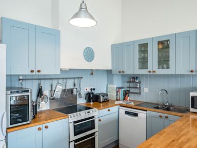 A kitchen with blue cabinets wooden countertops stove sink dishwasher and kitchen utensils at Slipway 12 in Rock