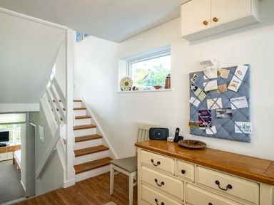 A hallway with wooden stairs a chair a dresser with items on top and a bulletin board on the wall at Slipway 12 in Rock