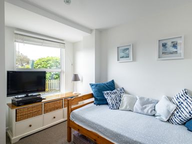 A small room with a wooden daybed covered in cushions and a cabinet with a TV and lamp near a window at Slipway 12 in Rock