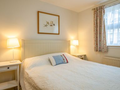 A bedroom with a bed a pillow two bedside tables with lamps a window with curtains and a framed picture at Slipway 12 Rock