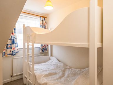 A bedroom with a white bunk bed near a window with patterned curtains at Slipway 12 in Rock