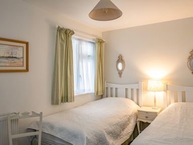 A bedroom with two single beds a bedside table and lamp a window with curtains and framed artwork at Slipway 12 Rock