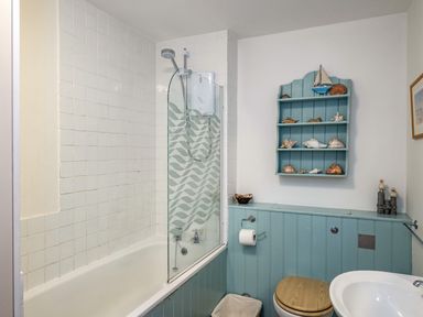 A bathroom with a bathtub and shower screen and a shelf with shells above a toilet at Slipway 12 in Rock