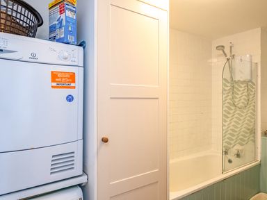 A bathroom with a washing machine, a white cabinet, and a bathtub with a shower and patterned glass screen at Slipway 12 in Rock
