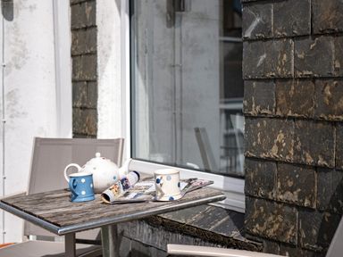 A patio table with two polka dot mugs a teapot and magazines next to a slate wall and window at Slipway 12 in Rock