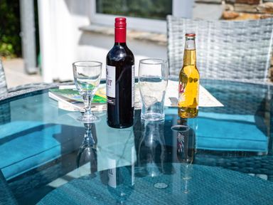A glass table with a bottle of wine a wine glass a beer bottle a pint glass and some books on an outdoor patio at Slipway 12 in Rock