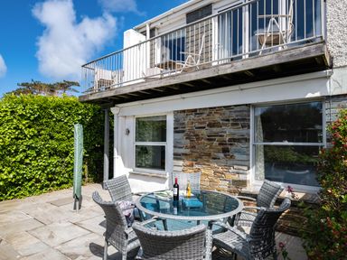 An outdoor patio with a glass table and six wicker chairs next to a two-story building with stone and white walls at Slipway 12 in Rock