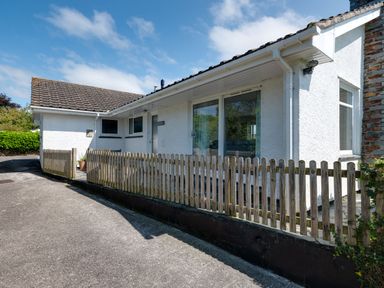 Exterior view of a white house with tiled roof and wooden fence along a driveway at Tremay Rock
