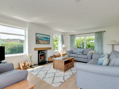 A living room with two gray sofas a wooden coffee table a rug a fireplace and windows with curtains at Tremay in Rock