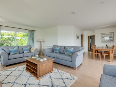 A living room with two gray sofas a wooden coffee table a floor lamp and a dining area with a wooden table and chairs at Tremay in Rock