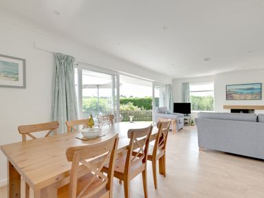 A dining table with six wooden chairs and a living room with grey sofas and a TV at Tremay in Rock