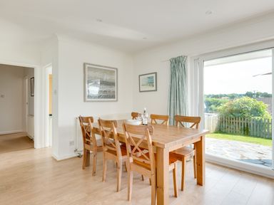 A dining room with a wooden table and six chairs and a large window showing a garden at Tremay in Rock