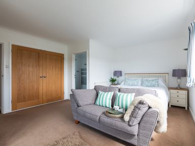 A bedroom with a bed two nightstands two lamps a gray sofa with pillows and a tray and wooden double closet doors at Tremay in Rock