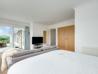 A bedroom with a bed a gray sofa a wall-mounted television wooden wardrobes and a sliding glass door leading outside at Tremay in Rock