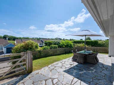 A stone patio with outdoor dining table and umbrella in a garden with wooden fence at Tremay in Rock
