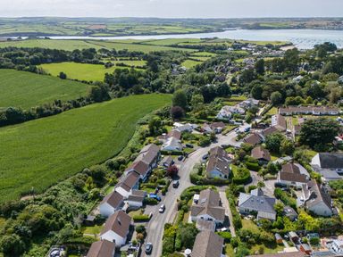 An aerial view of a residential neighborhood with houses and roads adjacent to green fields and a body of water at Tremay in Rock